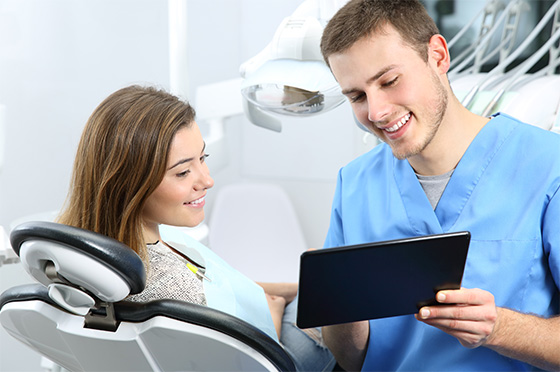 Young female dental patient brushing large model teeth with large toothbrush